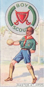 Carte de collection représentant un scout ayant le badge master-at-arms  armé d’un single stick et protégé d’un masque, ainsi qu’aux tibias (probablement venus d’une entreprise de chocolat britannique)